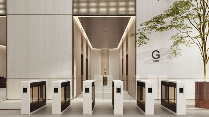 Hall d'entrée moderne du quartier O1NE, équipé de cinq tourniquets électroniques, avec des murs clairs, un arbre en pot et un panneau « G Floor » ; couloir avec une sculpture visible à l'arrière-plan.