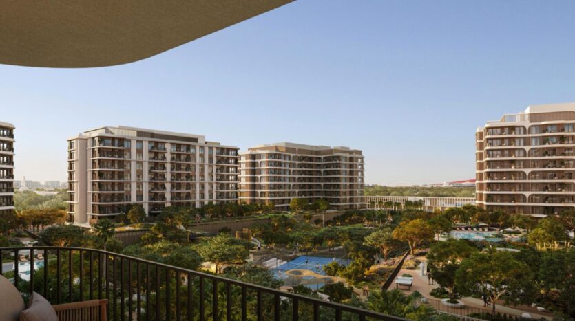 Vue depuis un balcon donnant sur les immeubles d'appartements modernes du complexe « The Canopies by Aldar », entourés d'arbres, d'une piscine et de terrains de sport, sous un ciel bleu limpide.