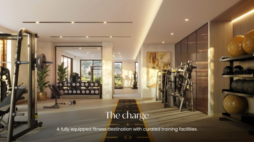 Salle de sport moderne dotée de grandes baies vitrées, de supports à haltères, d’appareils de musculation et d’un espace dédié aux étirements. Un éclairage chaleureux et une décoration aux tons neutres créent une ambiance idéale. Le texte indique : « The Charge. Un espace de remise en forme entièrement équipé, doté d’installations d’entraînement soigneusement sélectionnées, au sein du complexe The Canopies by Aldar. ».