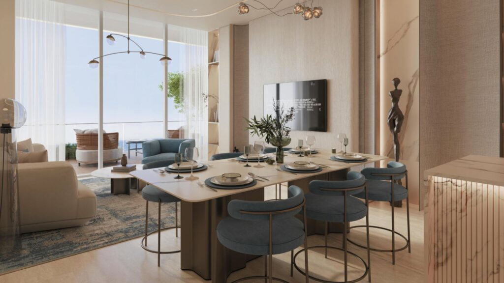 Une salle à manger moderne, avec une table dressée, des chaises rembourrées bleues et une statue abstraite, crée une ambiance raffinée au Vue Dorée. De grandes baies vitrées laissent entrer la lumière naturelle et offrent une vue sur le salon, agrémenté de canapés élégants et d'une plante en pot.