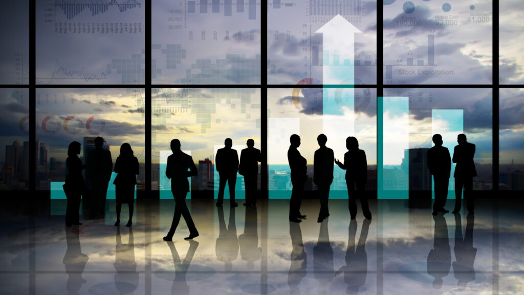 Des silhouettes d'hommes d'affaires se tiennent debout et discutent devant de grandes baies vitrées sur lesquelles sont superposés des graphiques et des tableaux, évoquant un cadre d'entreprise ou financier avec une vue sur le paysage urbain en arrière-plan. Cette scène souligne subtilement l’importance de se demander « Pourquoi il faut regarder qui investit avec vous à Dubaï », car il est essentiel de bien connaître ses partenaires d’investissement dans des environnements aussi dynamiques.
