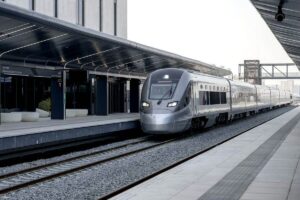 Un train à grande vitesse Etihad Rail moderne, de couleur argentée, est à l'arrêt sur un quai couvert aux lignes épurées, dans une gare contemporaine d'Abou Dhabi aux éléments de design minimalistes.
